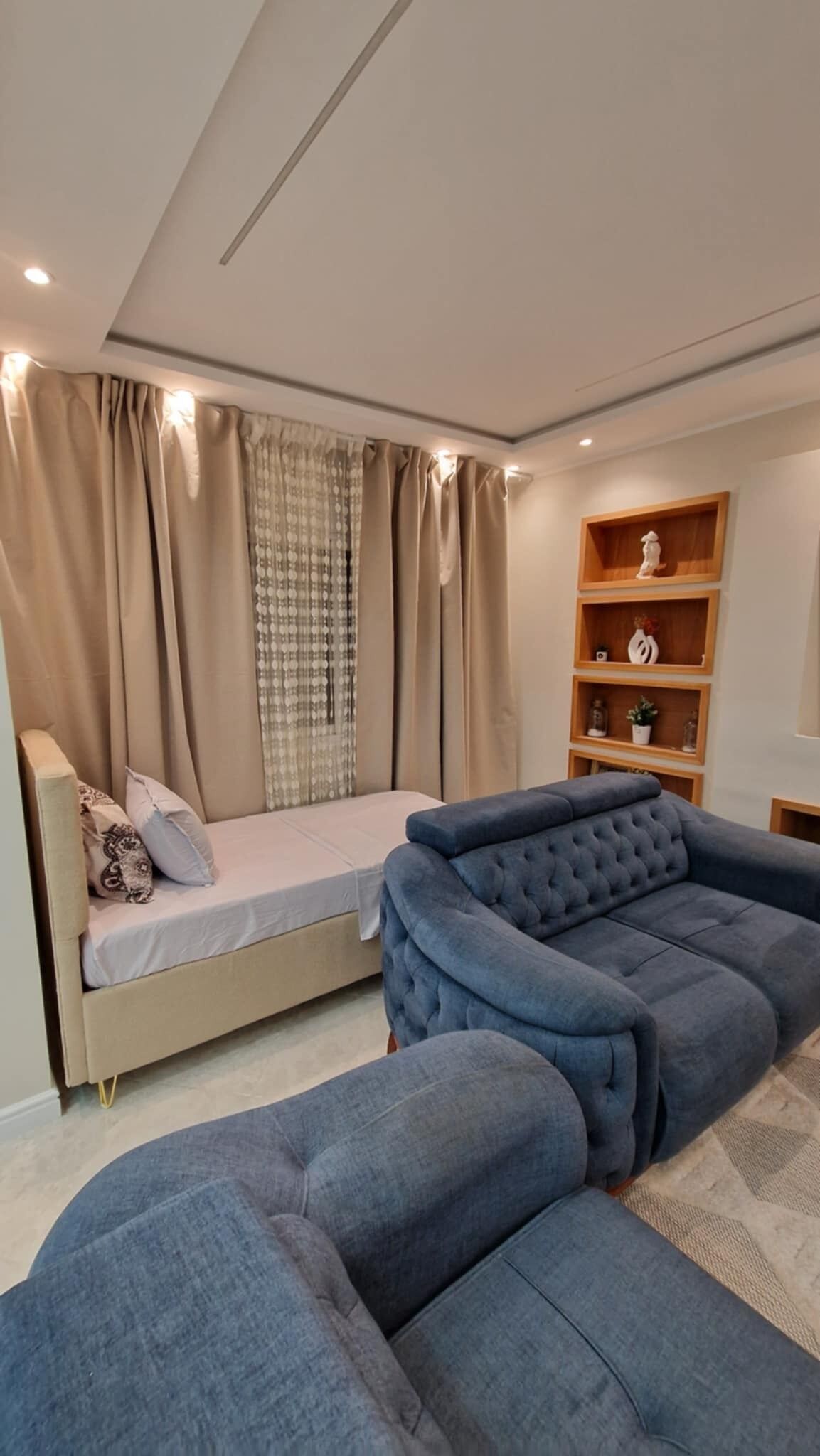 A modern bedroom with a bed, a blue sofa, and a wooden shelf unit.