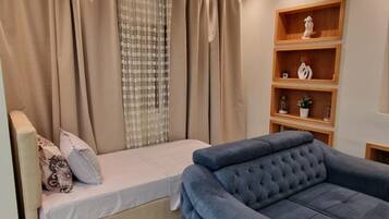 A modern bedroom with a bed, a blue sofa, and a wooden shelf unit.