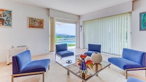 A modern living room with two blue sofas, a glass coffee table, and a view of a pool and mountains through large windows.