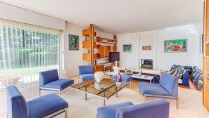A modern living room with blue sofas, a glass coffee table, and a bookshelf.