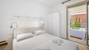 Ein Hotelzimmer mit Bett, Kleiderschrank, Nachttisch, Lampe und einer Schiebeglastür nach draußen.