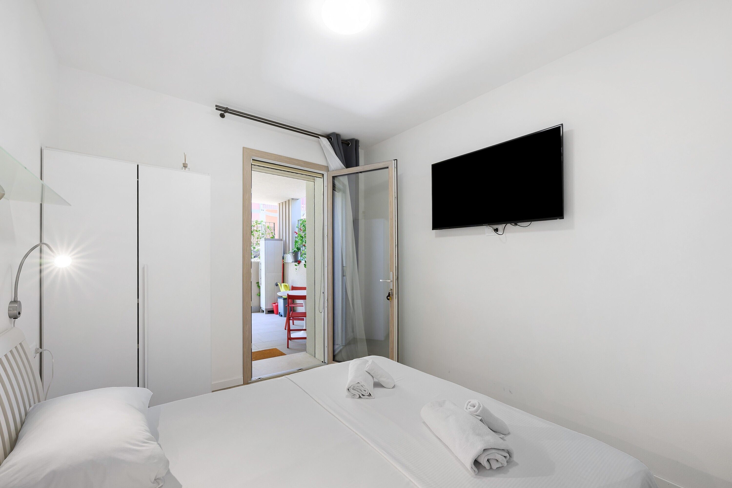 Ein Hotelzimmer mit Bett, Wand-Fernseher, Kleiderschrank und einer Tür zum Balkon.