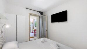 Ein Hotelzimmer mit Bett, Wand-Fernseher, Kleiderschrank und einer Tür zum Balkon.