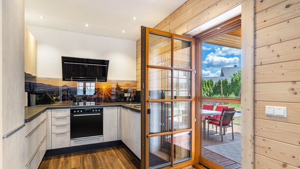 A modern kitchen with wooden cabinetry, a built-in oven, and a sliding glass door leading to an outdoor seating area. - Holiday Home 'Ferienhaus Traum Teufel' with Terrace, Garden and Wi-Fi (Hettingen)