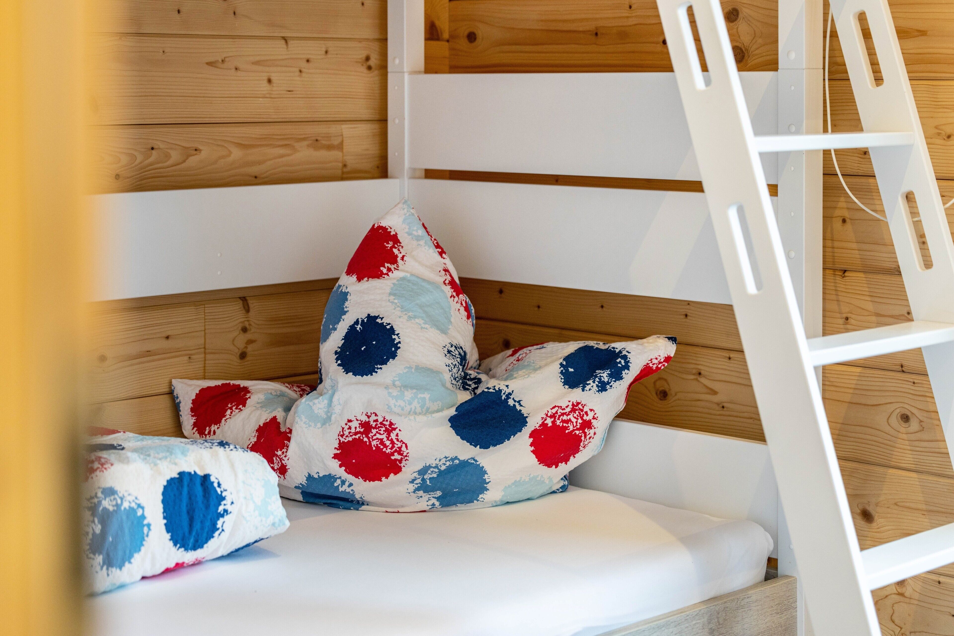 A corner of a room with a white sofa, a white ladder, and a wooden wall.