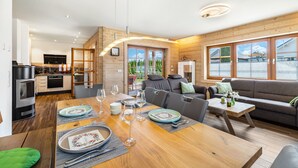 A modern kitchen with a built-in oven, a dining area with a wooden table set for a meal, and a cozy living area with a sofa and a coffee table. - Holiday Home 'Ferienhaus Traum Teufel' with Terrace, Garden and Wi-Fi (Hettingen)