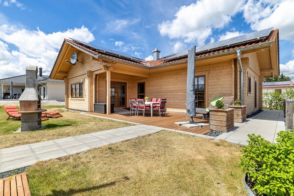 Ein Holzhaus mit Terrasse, Sitzgelegenheiten im Freien und einem Schornstein.