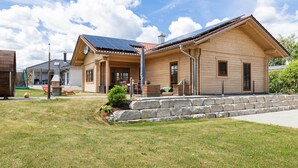 A wooden house with a sloped roof, solar panels, and a stone retaining wall. - Holiday Home 'Ferienhaus Traum Teufel' with Terrace, Garden and Wi-Fi (Hettingen)