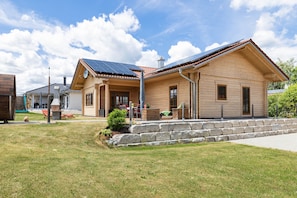 Ein Haus aus Holz mit einem geneigten Dach, Solaranlagen und einer Steinmauer.