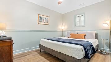 Une chambre à coucher avec un lit, une table de chevet en bois, un ventilateur de plafond, des lampes fixées au mur et un tableau encadré.