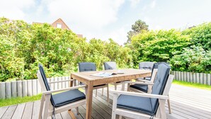 A wooden deck with a table and chairs, surrounded by lush greenery and a wooden fence. - F27 Living Whg. 01 - Sylt (Sylt)