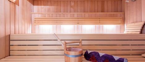 A wooden sauna with benches, a wooden bucket, and a rolled-up towel.