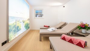 Une chambre avec deux lits, une fenêtre donnant sur la plage, une petite fenêtre et une plante posée sur une table d’appoint.