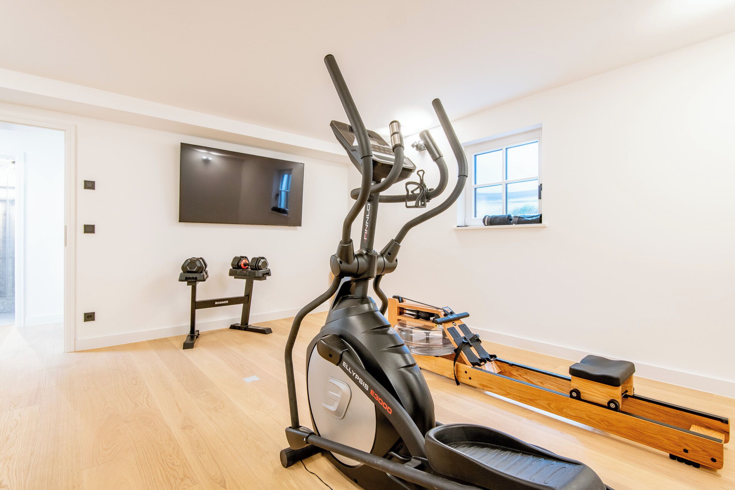 Ett hemmagym med en crosstrainer, en roddmaskin och hantlar.
