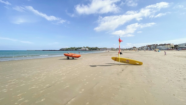 Een strand met strandwachtattributen, waaronder een geel surfboard en een opblaasbare reddingsboot in oranje.