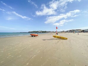 Ein Strand mit Rettungsausrüstung, darunter ein gelbes Surfbrett und ein orangefarbenes Rettungsboot.