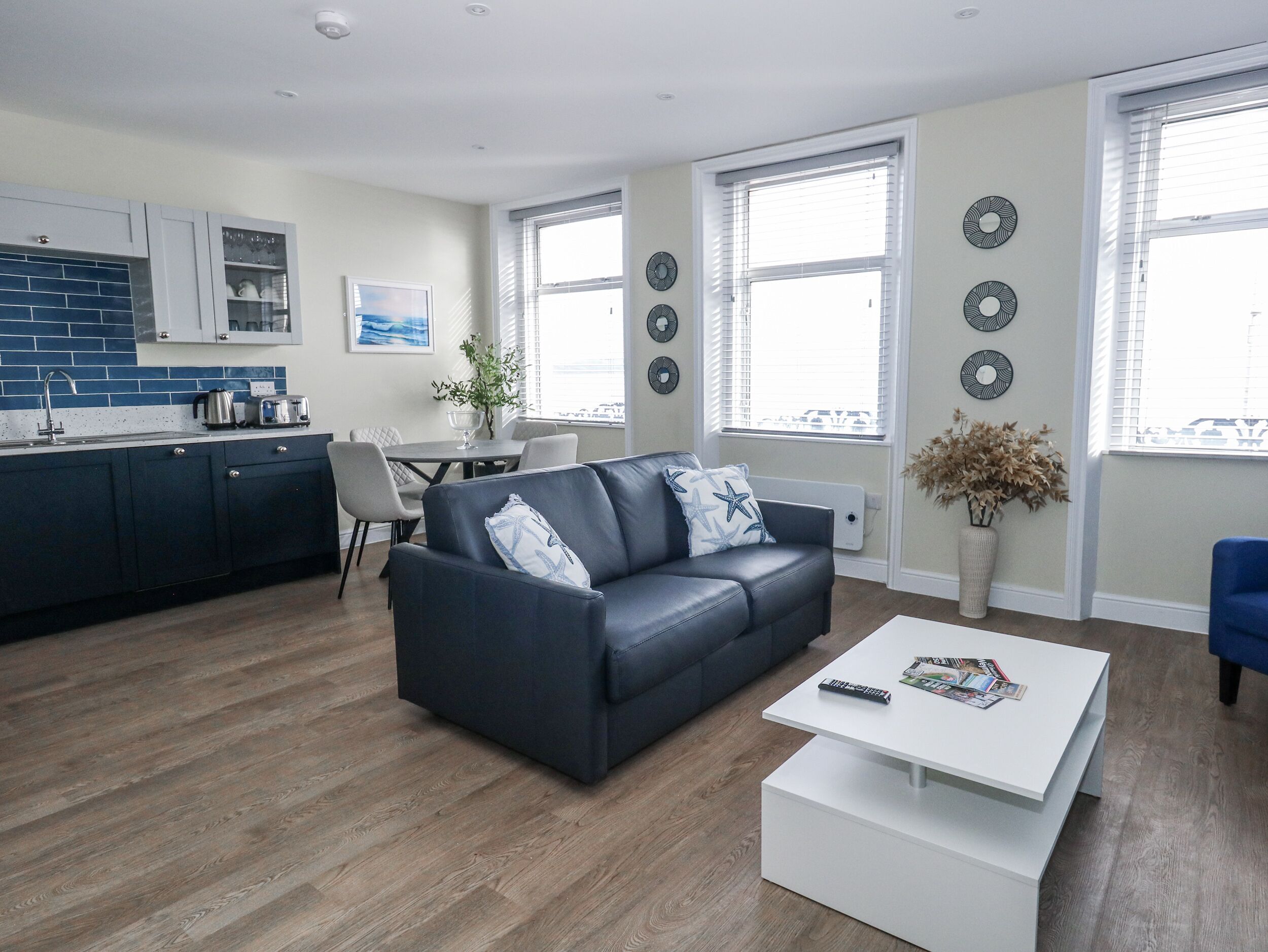 A modern living room with a dark blue sofa, a white coffee table, and a dining area with a table and chairs.