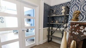 Une pièce avec une porte blanche, un mur orné d’un motif bleu, une cheminée en briques et un plancher en bois.