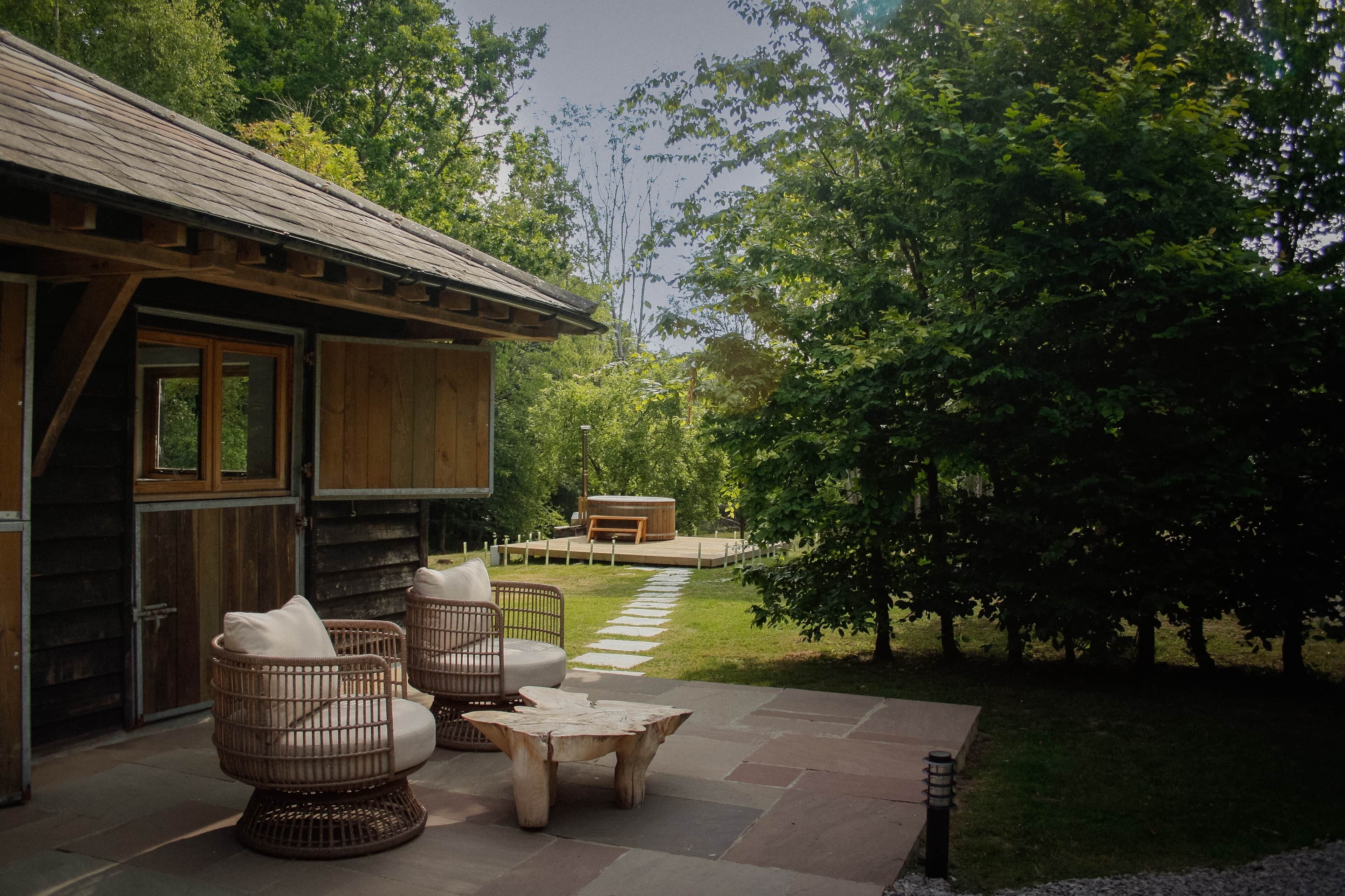 A wooden cabin with wicker furniture, a stone patio, and a garden path.