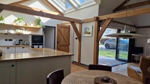 A modern kitchen with skylights, wooden beams, and a dining area with a table and chairs. - The Stable | Oak-Frame Kent hideaway · Hot Tub (Cranbrook)