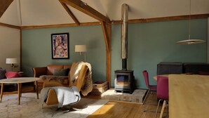 A cozy living room with a fireplace, a sofa, a chair, and a table. - The Stable | Oak-Frame Kent hideaway · Hot Tub (Cranbrook)