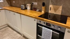 A kitchen with white cabinets, a wooden countertop, a built-in stove, and a coffee maker. - Napton on the Hill - Sleeps Upto 7 & Pet Friendly (Southam)