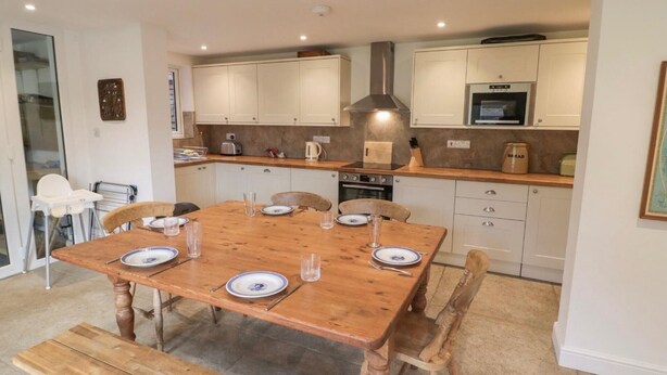 A modern kitchen with white cabinets, a built-in oven, and a microwave. There is a wooden dining table with chairs and a bench. - Napton on the Hill - Sleeps Upto 7 & Pet Friendly (Southam)