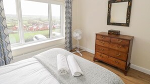 A bedroom with a large window, a wooden dresser, and a bed with rolled towels. - Napton on the Hill - Sleeps Upto 7 & Pet Friendly (Southam)