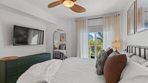 Une chambre à coucher avec un lit, une télévision, une commode, un miroir et une fenêtre avec des rideaux.