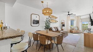 A modern dining area with a wooden table and wicker chairs, a ceiling fan, and a view of the outdoors. - August Beach Escape – Special Rates Available! (Treasure Island)