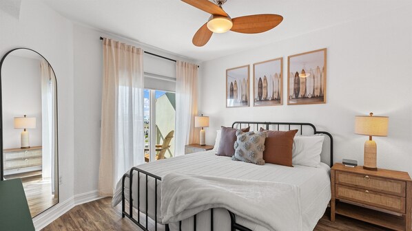 Une chambre à coucher comprenant un lit, des tables de chevet, un ventilateur de plafond et une grande fenêtre avec des rideaux.
