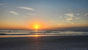 A beach at sunset with the sun low on the horizon, calm sea, and a clear sky. - August Beach Escape – Special Rates Available! (Treasure Island)