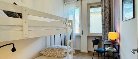 A bunk bed with a pillow, a desk with a chair, a lamp, and a window with curtains.