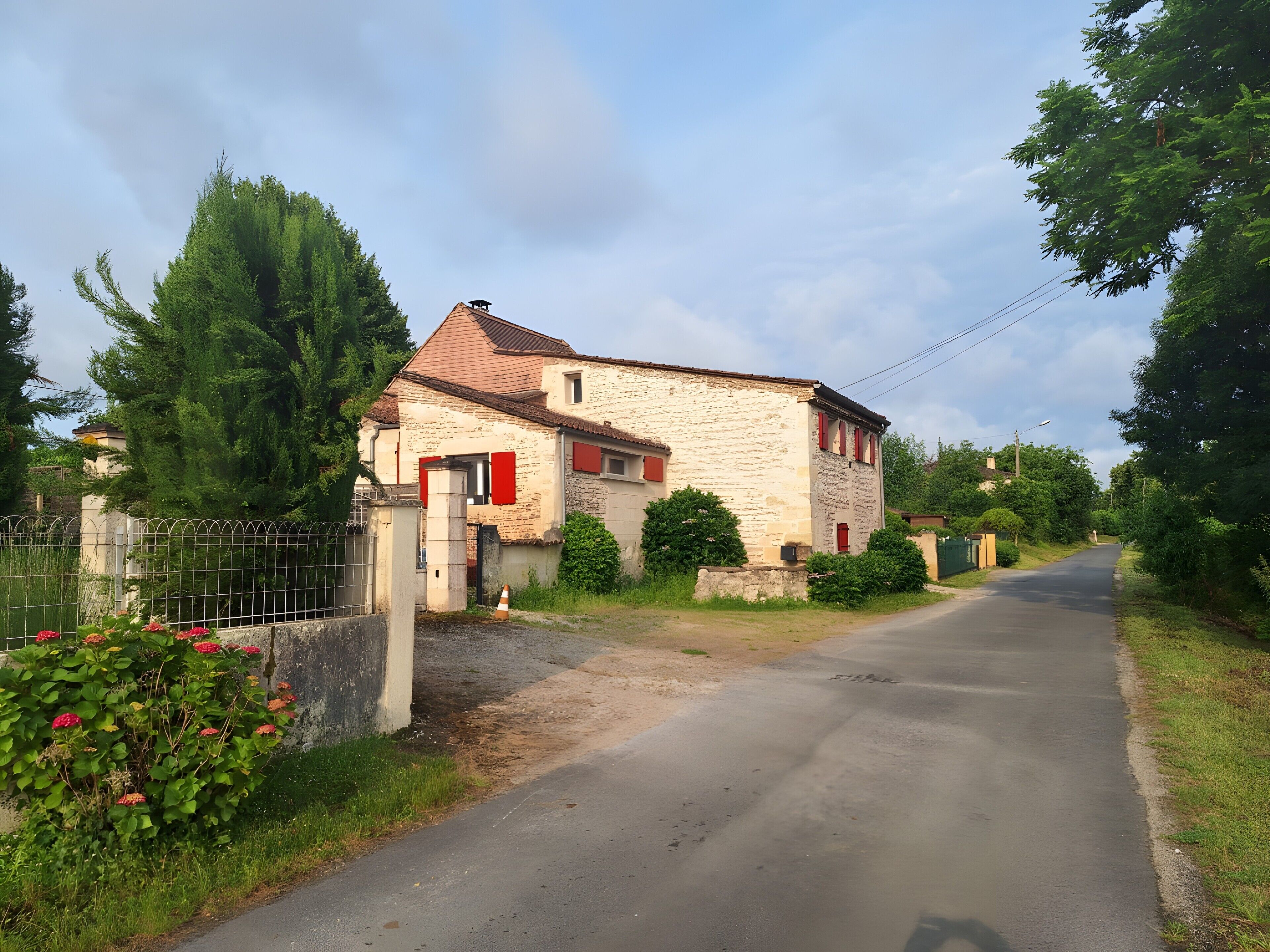 Ein Feldweg führt zu einem Steinhaus mit roter Tür und Fensterläden.