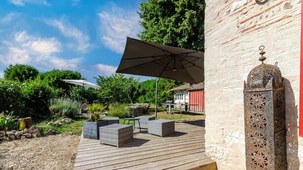 Une terrasse en bois avec des meubles d’extérieur, un grand parasol et une lanterne décorative en métal.