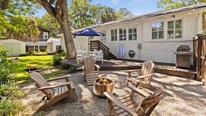 Eine Terrasse mit Adirondack-Stühlen, einem Feuerkorb und einem Grill.