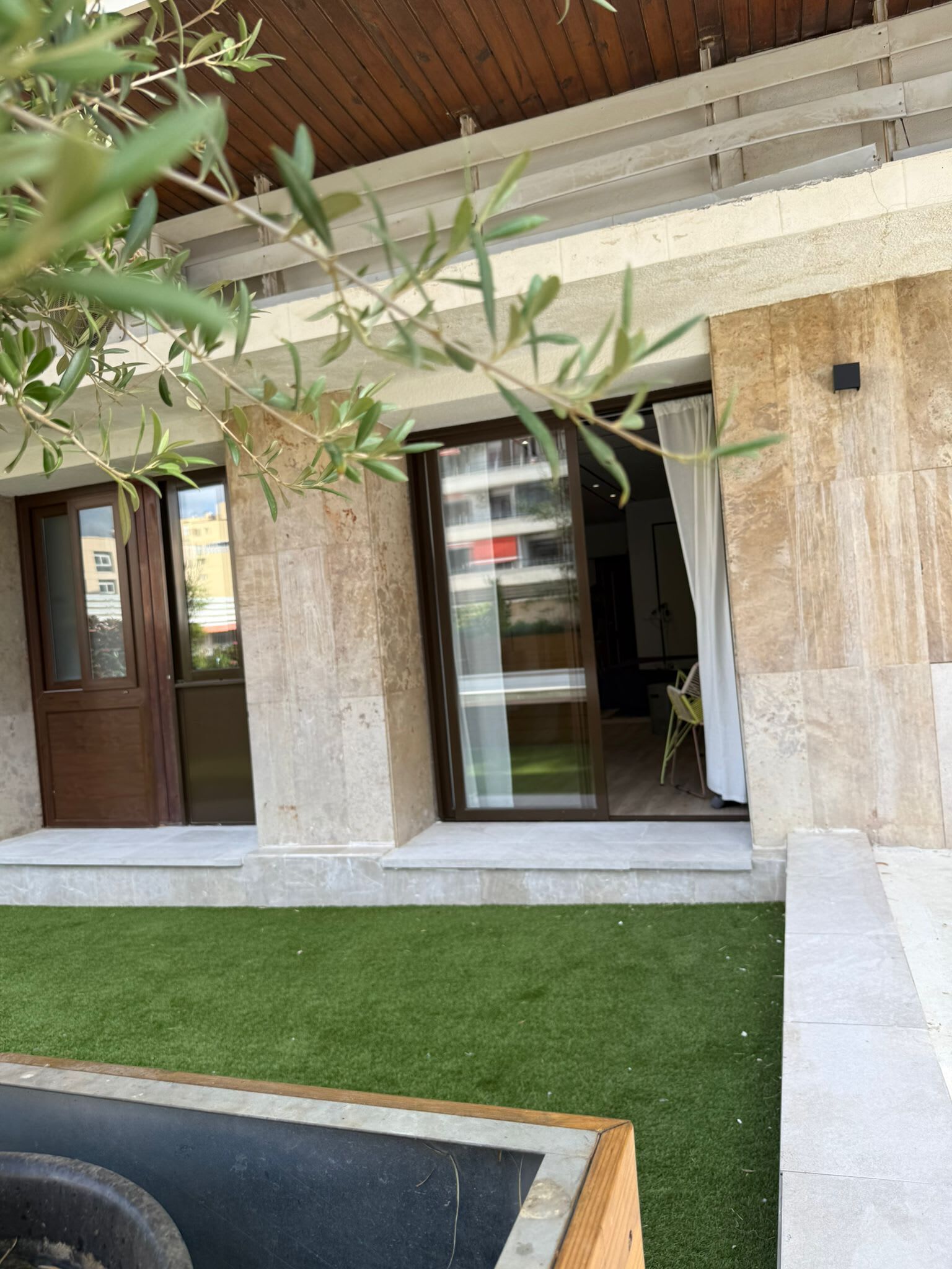 A modern building with a wooden ceiling, large glass doors, and a small outdoor area with artificial grass.