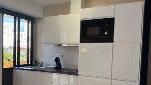 A modern kitchen with white cabinets, a black microwave, and a window with a view of buildings.