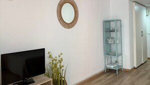 A modern living room with a flat-screen TV, a woven basket with plants, a glass cabinet, and a white wall with a circular mirror. - Charming Studio in La Nogalera, Near Beach (Torremolinos)