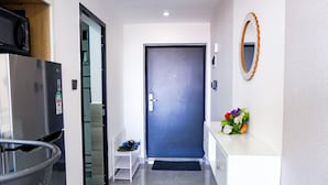 Un couloir moderne avec une porte bleu foncé, une console blanche agrémentée d’un miroir et une petite étagère où sont posées des chaussures.