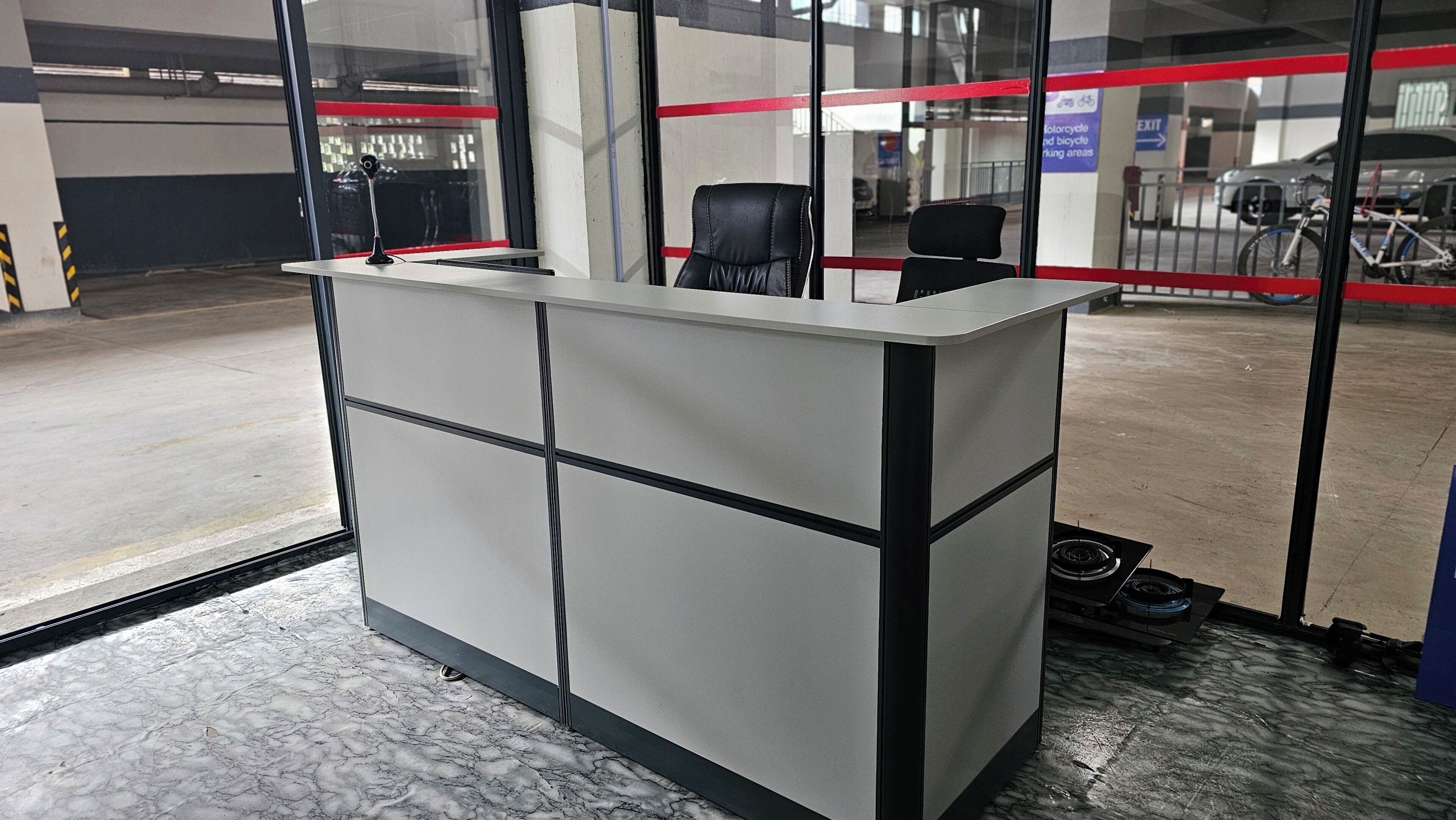 A reception desk with a glass partition, a chair, and a sign indicating motorcycle and bicycle parking areas.