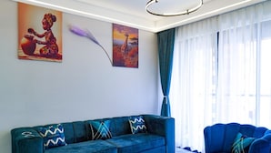 Un salon avec un canapé bleu, une table basse sur laquelle on voit des fruits, et deux tableaux accrochés au mur.