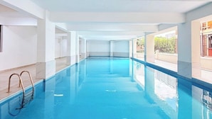 Une grande piscine intérieure à l’eau d’un bleu limpide, entourée de murs et de colonnes blancs.
