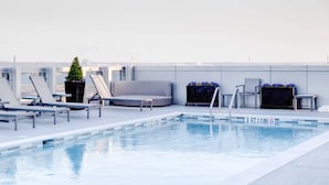 Un espace piscine aménagé sur le toit, avec des chaises longues, un canapé et une petite table.