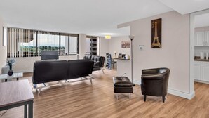 Un salon moderne avec un canapé, une petite table et un fauteuil. Il y a une grande fenêtre avec des stores, une bibliothèque et un tableau représentant la Tour Eiffel.