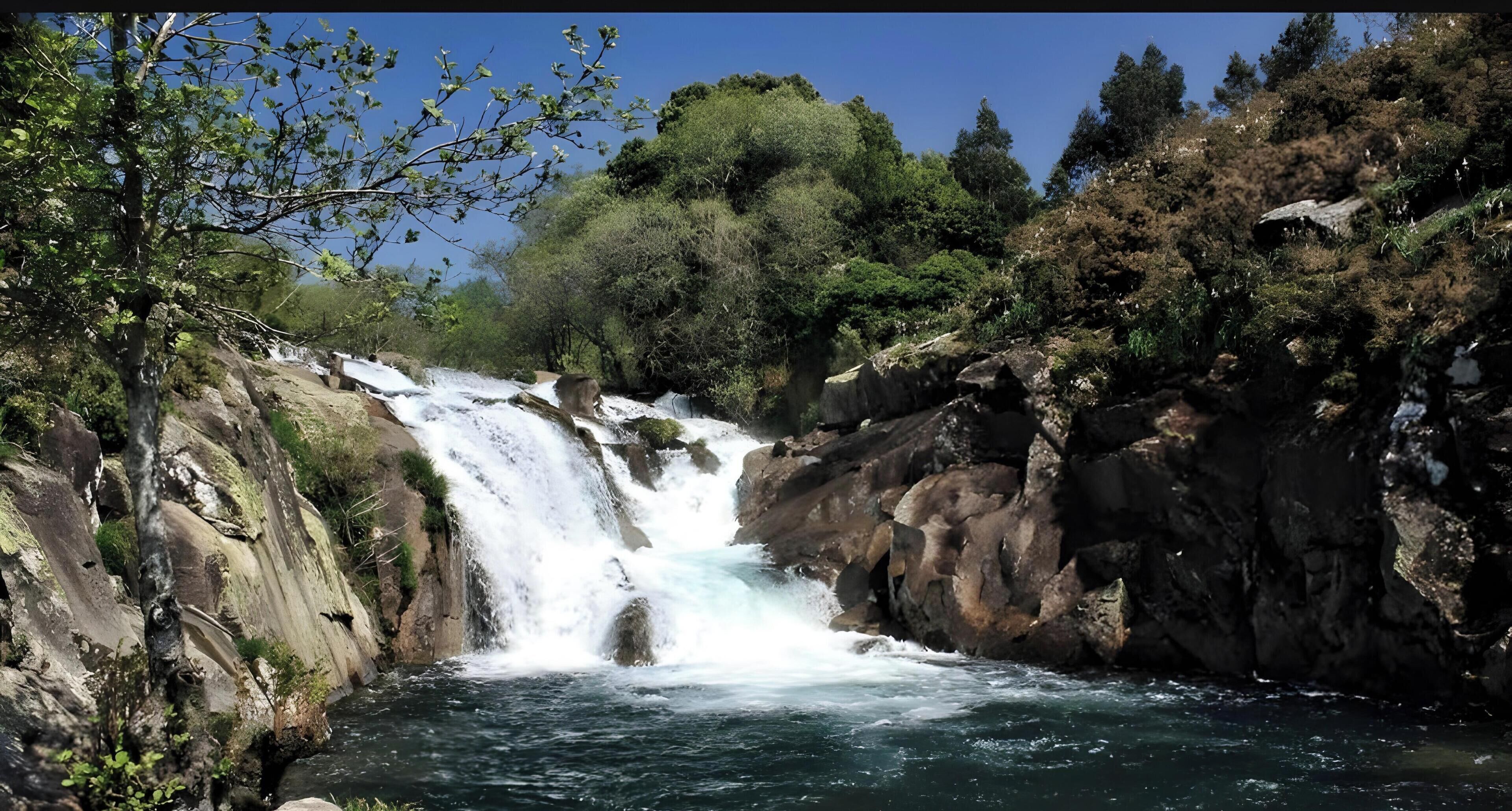 Una cascada rodeada de terreno rocoso y vegetación densa.