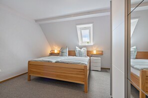 Ein Schlafzimmer mit einem hölzernen Bett, Nachttischen, einem kleinen Fenster und einem Spiegel.