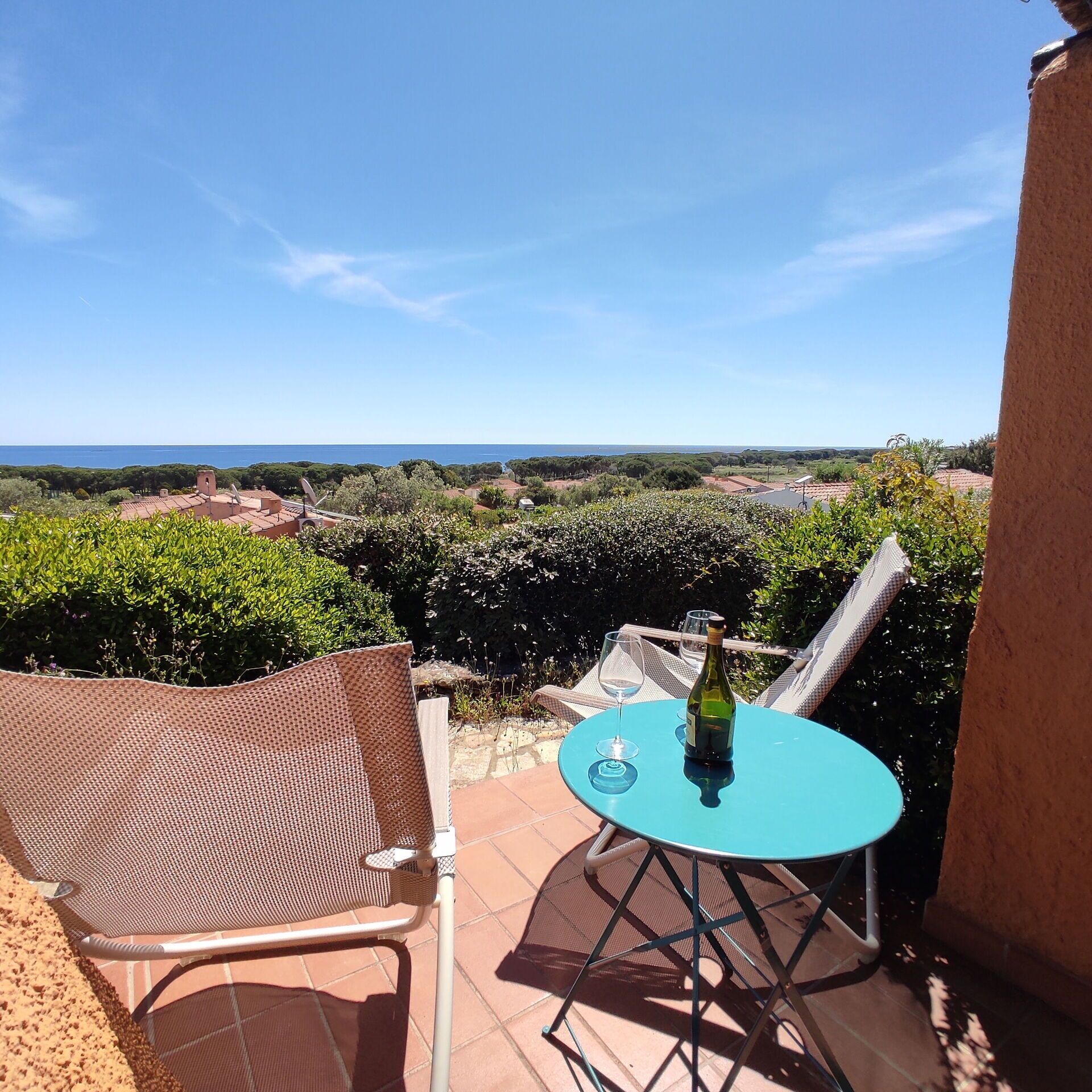 Une terrasse avec une table et des chaises, une bouteille de vin et une vue sur la mer et la verdure.