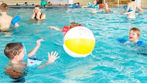 An indoor swimming pool with multiple people swimming and playing.