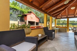 An outdoor patio with wicker furniture, a stone table, and a red barbecue grill.